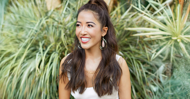 Susie Ma smiling outdoors with green plants in the background